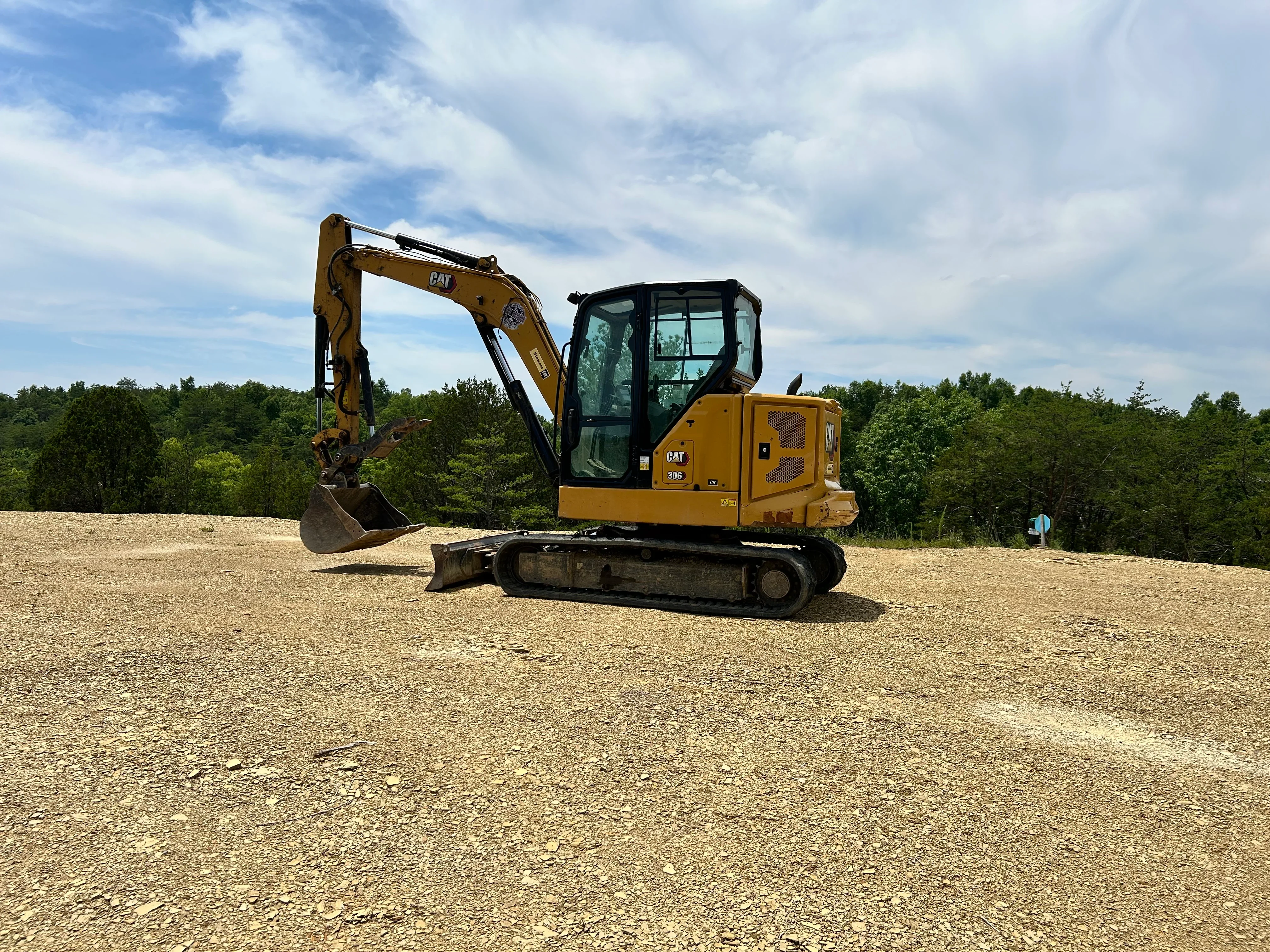 CAT 390 excavator with bucket on graded gravel lot, wooded background